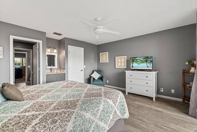 bedroom featuring ceiling fan, sink, light hardwood / wood-style flooring, a textured ceiling, and connected bathroom