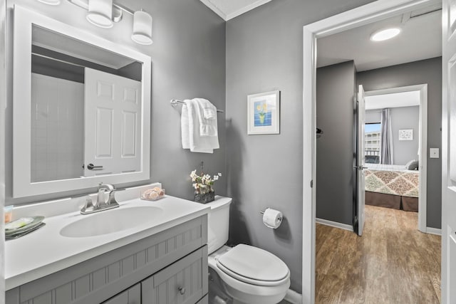 bathroom featuring toilet, ornamental molding, wood-type flooring, and vanity