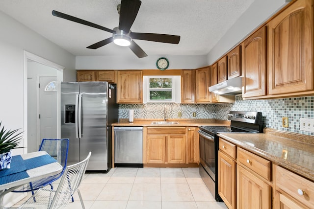 kitchen featuring stainless steel appliances, tasteful backsplash, light tile patterned flooring, a sink, and under cabinet range hood