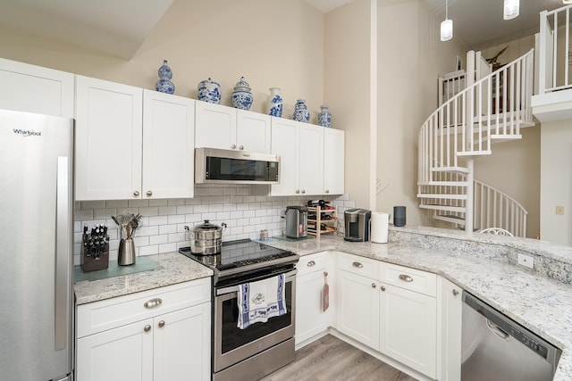 kitchen with white cabinetry, stainless steel appliances, light stone countertops, and decorative backsplash