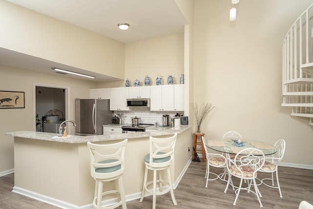 kitchen with a kitchen bar, white cabinetry, light wood-type flooring, kitchen peninsula, and stainless steel appliances