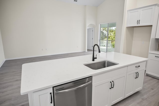 kitchen featuring light wood-type flooring, stainless steel dishwasher, sink, white cabinetry, and an island with sink