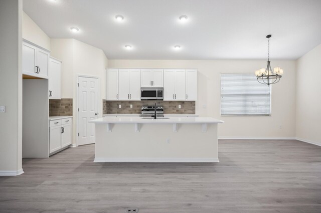 kitchen with appliances with stainless steel finishes, a center island with sink, an inviting chandelier, white cabinets, and light hardwood / wood-style floors