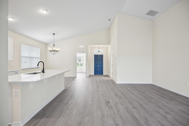 kitchen with vaulted ceiling, sink, pendant lighting, light hardwood / wood-style floors, and white cabinetry