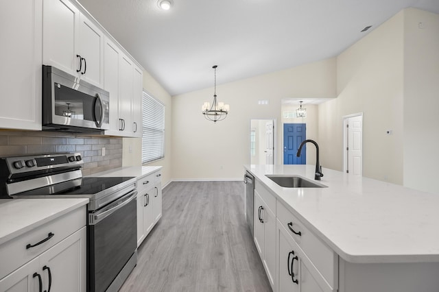 kitchen featuring stainless steel appliances, vaulted ceiling, sink, a center island with sink, and a notable chandelier