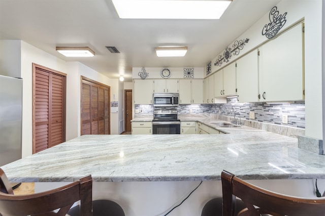 kitchen with kitchen peninsula, appliances with stainless steel finishes, backsplash, a breakfast bar, and sink