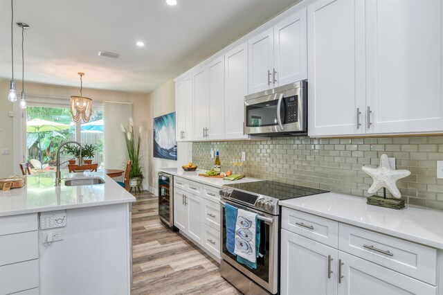 kitchen with appliances with stainless steel finishes, sink, white cabinets, light hardwood / wood-style floors, and hanging light fixtures