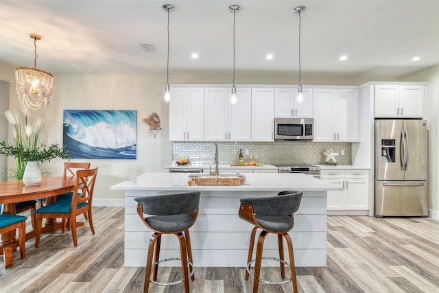 kitchen featuring white cabinets, decorative light fixtures, stainless steel appliances, and light hardwood / wood-style flooring