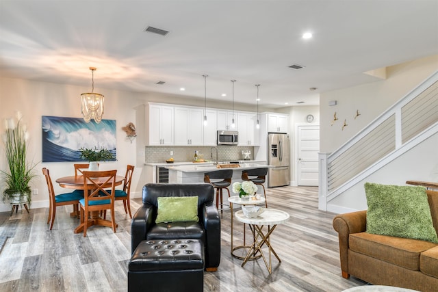 living room featuring an inviting chandelier, light hardwood / wood-style flooring, beverage cooler, and sink