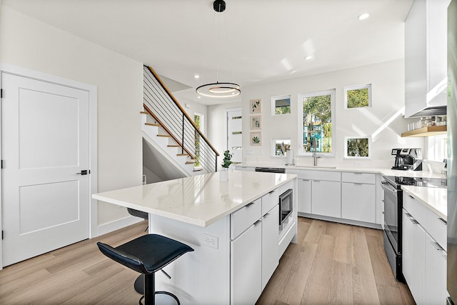 kitchen with white cabinetry, hanging light fixtures, black electric range, light hardwood / wood-style floors, and a kitchen island