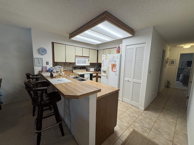 kitchen with white appliances, light tile patterned floors, a breakfast bar, a peninsula, and wooden counters