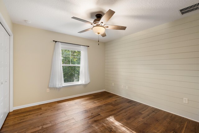 unfurnished room with ceiling fan, wooden walls, dark wood-type flooring, and a textured ceiling