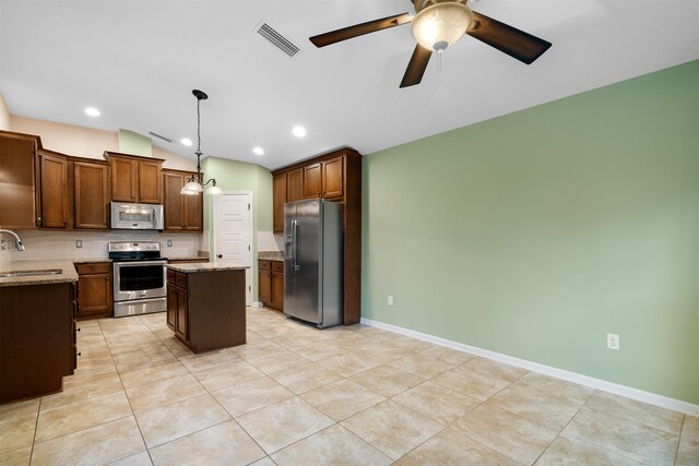 kitchen with pendant lighting, sink, a kitchen island, light stone counters, and stainless steel appliances