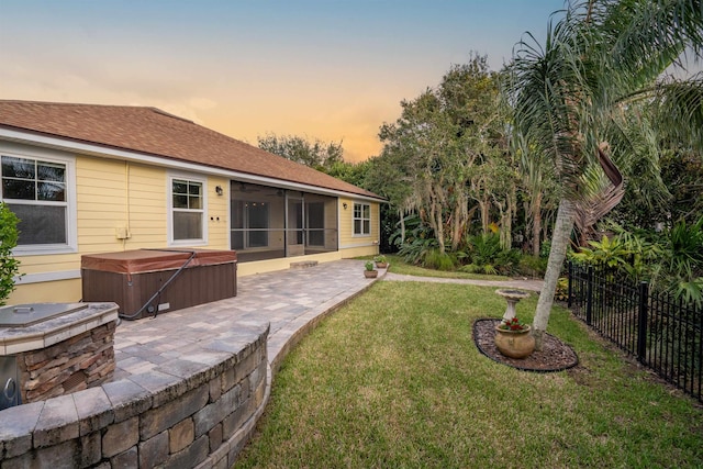 yard at dusk featuring a sunroom, a patio, and a hot tub