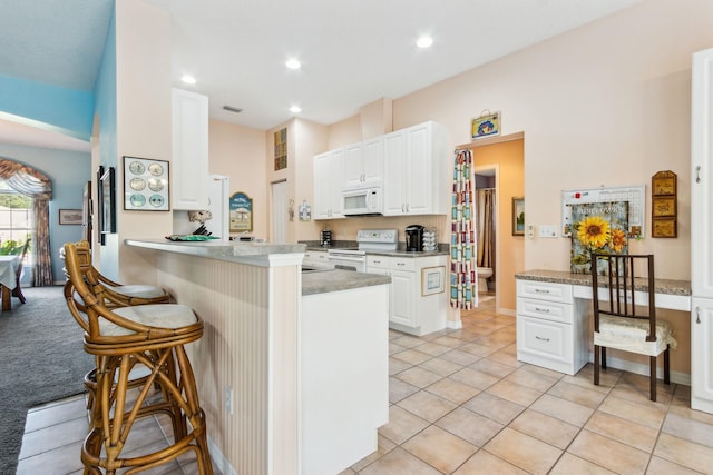 kitchen with kitchen peninsula, a kitchen breakfast bar, white appliances, and white cabinets