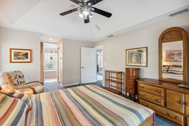 carpeted bedroom with a tray ceiling, ensuite bath, ceiling fan, and multiple windows