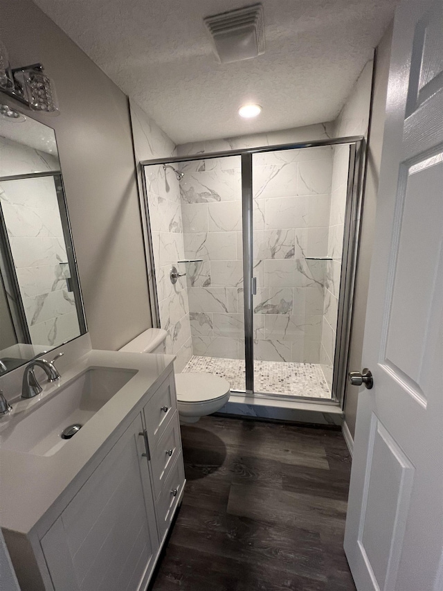 bathroom with toilet, a shower with shower door, wood-type flooring, a textured ceiling, and vanity