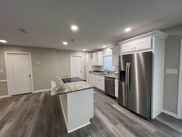 kitchen with appliances with stainless steel finishes, light stone counters, white cabinetry, and a center island