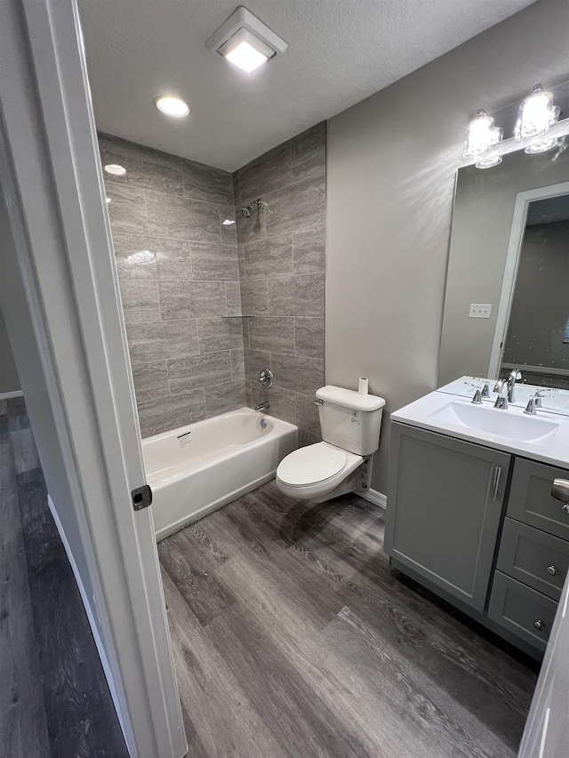 full bathroom featuring toilet, tiled shower / bath combo, hardwood / wood-style floors, a textured ceiling, and vanity