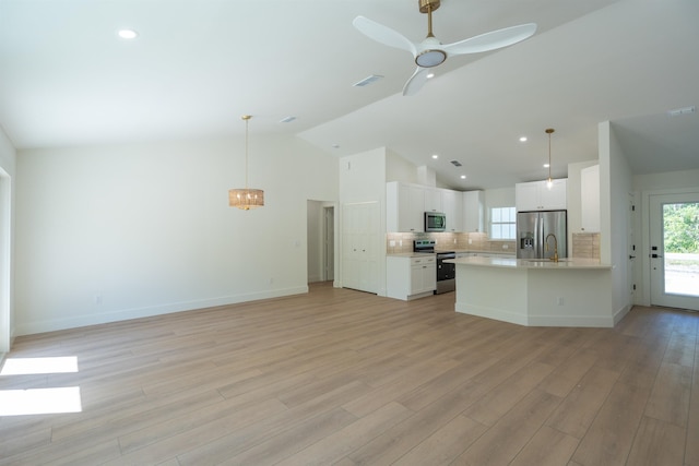 kitchen featuring open floor plan, stainless steel appliances, light countertops, decorative light fixtures, and white cabinets