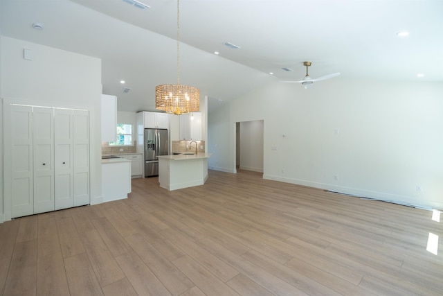 unfurnished living room with lofted ceiling, visible vents, a sink, light wood-style flooring, and ceiling fan with notable chandelier