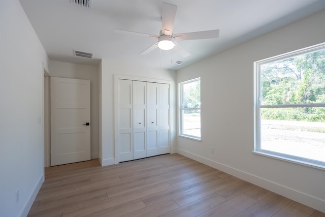 unfurnished bedroom with light wood-type flooring, visible vents, baseboards, and multiple windows