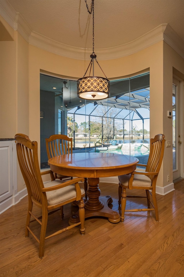 dining room featuring ornamental molding, a sunroom, baseboards, and light wood finished floors