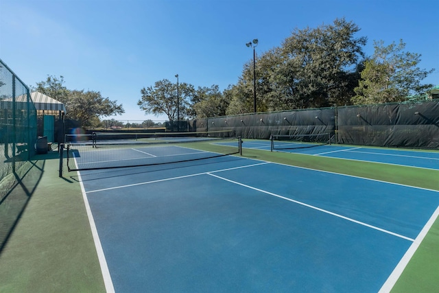 view of tennis court with community basketball court and fence