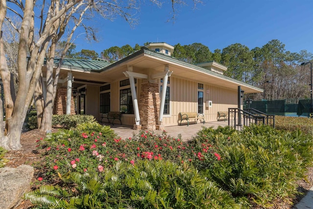 view of home's exterior with stone siding, a standing seam roof, fence, a patio area, and board and batten siding