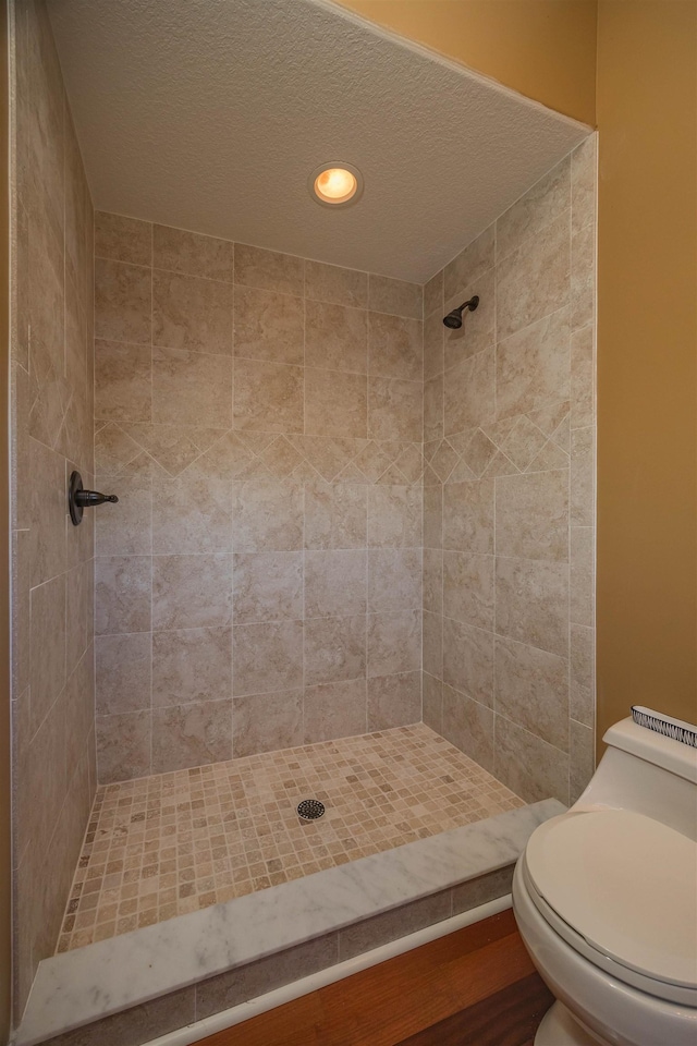 full bath featuring recessed lighting, a tile shower, a textured ceiling, and toilet