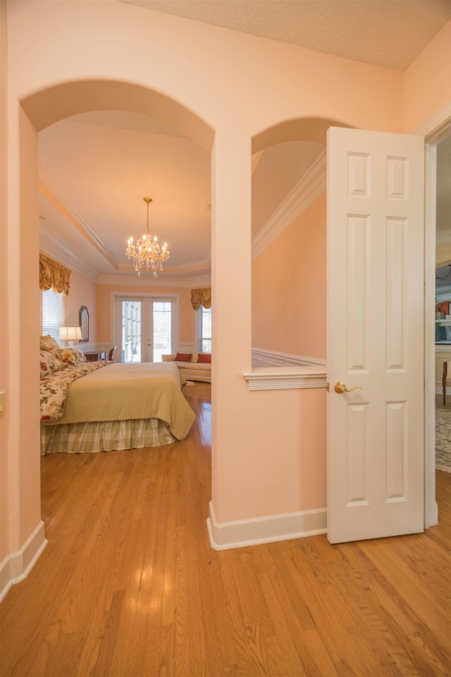 unfurnished bedroom with arched walkways, a notable chandelier, wood finished floors, baseboards, and crown molding