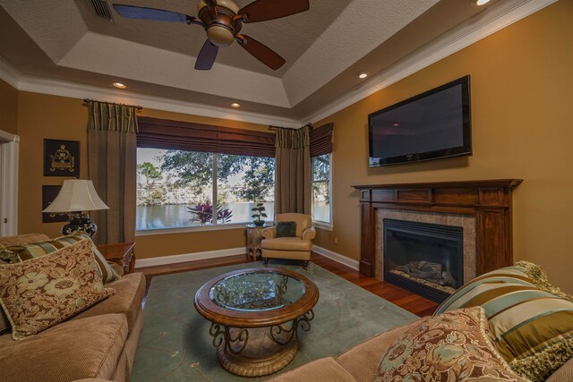 living area featuring a raised ceiling, a tiled fireplace, ornamental molding, wood finished floors, and baseboards