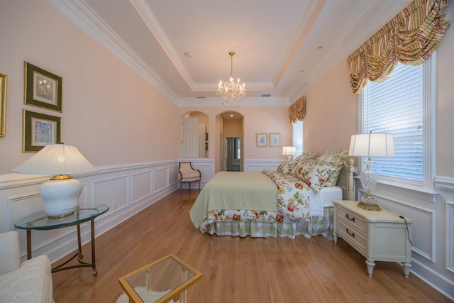 bedroom with arched walkways, a decorative wall, wood finished floors, a tray ceiling, and crown molding