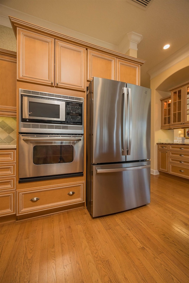 kitchen with recessed lighting, appliances with stainless steel finishes, glass insert cabinets, light wood-style floors, and ornamental molding