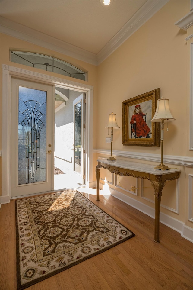 foyer entrance with wood finished floors, crown molding, and wainscoting