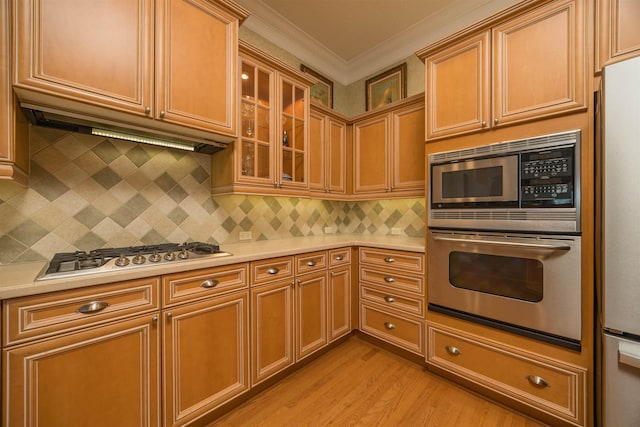 kitchen with light wood finished floors, glass insert cabinets, stainless steel appliances, crown molding, and light countertops