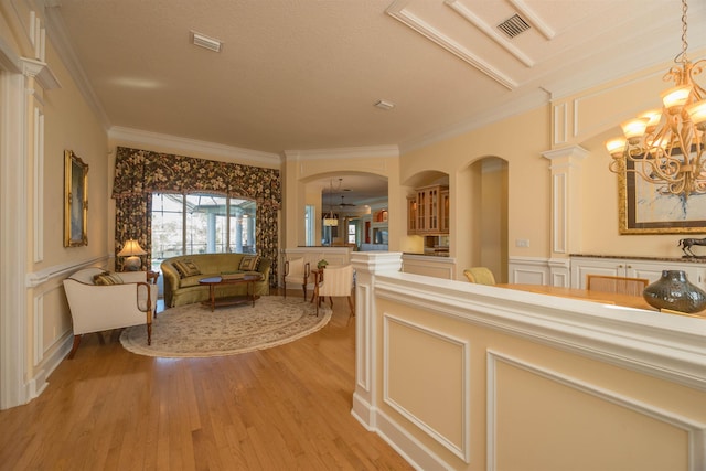 hall with visible vents, a decorative wall, an inviting chandelier, ornamental molding, and light wood-style floors