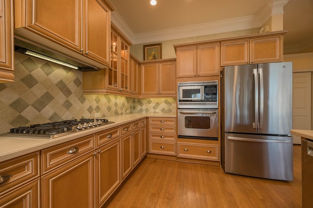 kitchen featuring light wood finished floors, stainless steel appliances, light countertops, ornamental molding, and glass insert cabinets