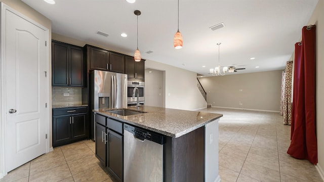 kitchen featuring pendant lighting, ceiling fan with notable chandelier, decorative backsplash, an island with sink, and appliances with stainless steel finishes