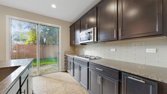 kitchen featuring light stone countertops, backsplash, dark brown cabinets, stainless steel appliances, and light tile patterned flooring