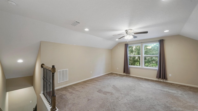 additional living space with a textured ceiling, ceiling fan, light colored carpet, and vaulted ceiling