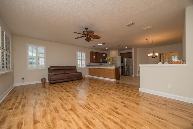 unfurnished living room featuring ceiling fan with notable chandelier, light hardwood / wood-style floors, and a textured ceiling