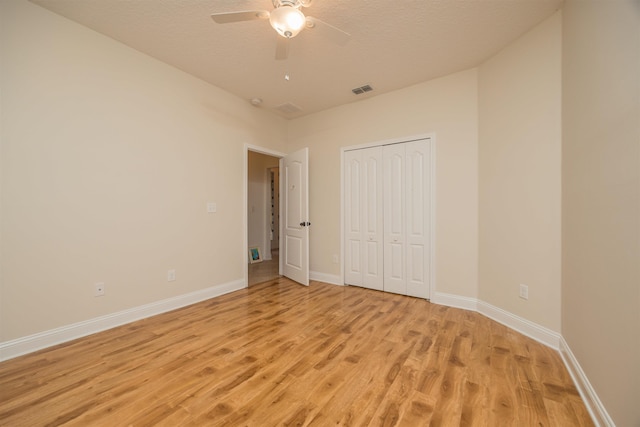 unfurnished bedroom with a textured ceiling, a closet, light hardwood / wood-style floors, and ceiling fan