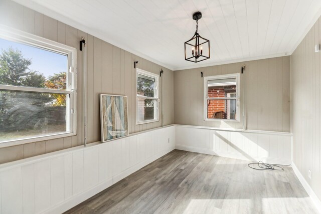 unfurnished dining area with hardwood / wood-style flooring, crown molding, a wealth of natural light, and a chandelier