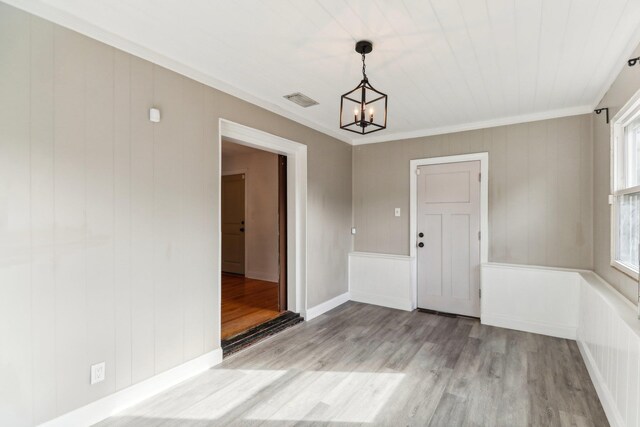 unfurnished dining area featuring light hardwood / wood-style floors, ornamental molding, and a notable chandelier