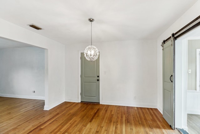 unfurnished room with a barn door, light hardwood / wood-style flooring, and a notable chandelier