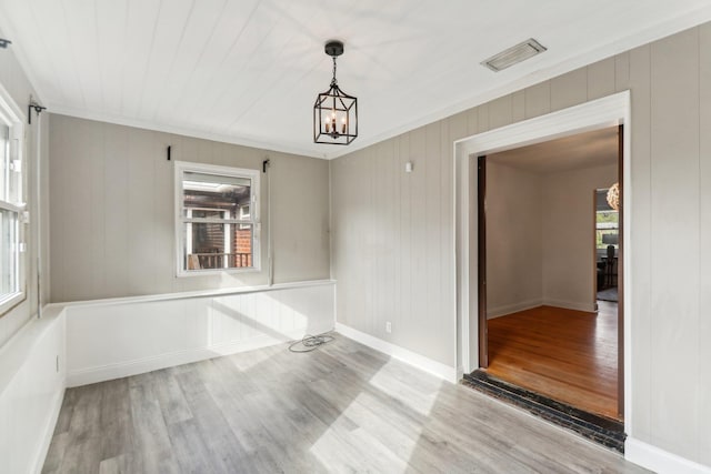 unfurnished room with hardwood / wood-style flooring, wood walls, ornamental molding, and an inviting chandelier