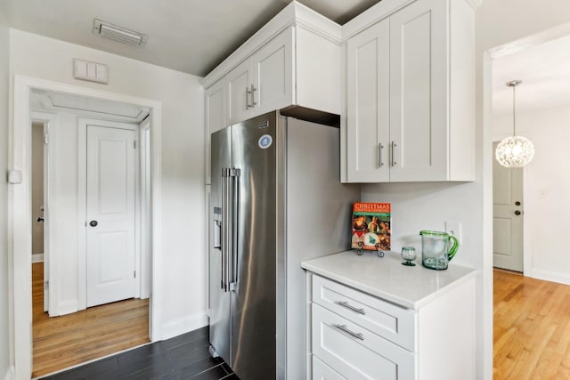 kitchen with an inviting chandelier, pendant lighting, wood-type flooring, high quality fridge, and white cabinets