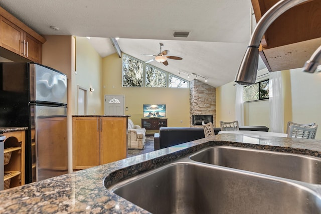 kitchen featuring a fireplace, a healthy amount of sunlight, stainless steel refrigerator, and lofted ceiling