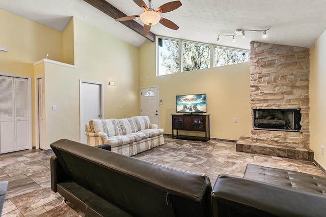 living room featuring high vaulted ceiling, a stone fireplace, rail lighting, ceiling fan, and a textured ceiling